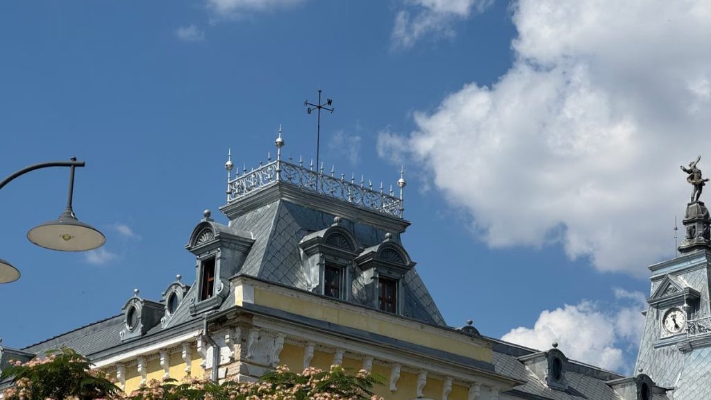 Ornate historical building with weather vane and clock tower under a clear blue sky with clouds.